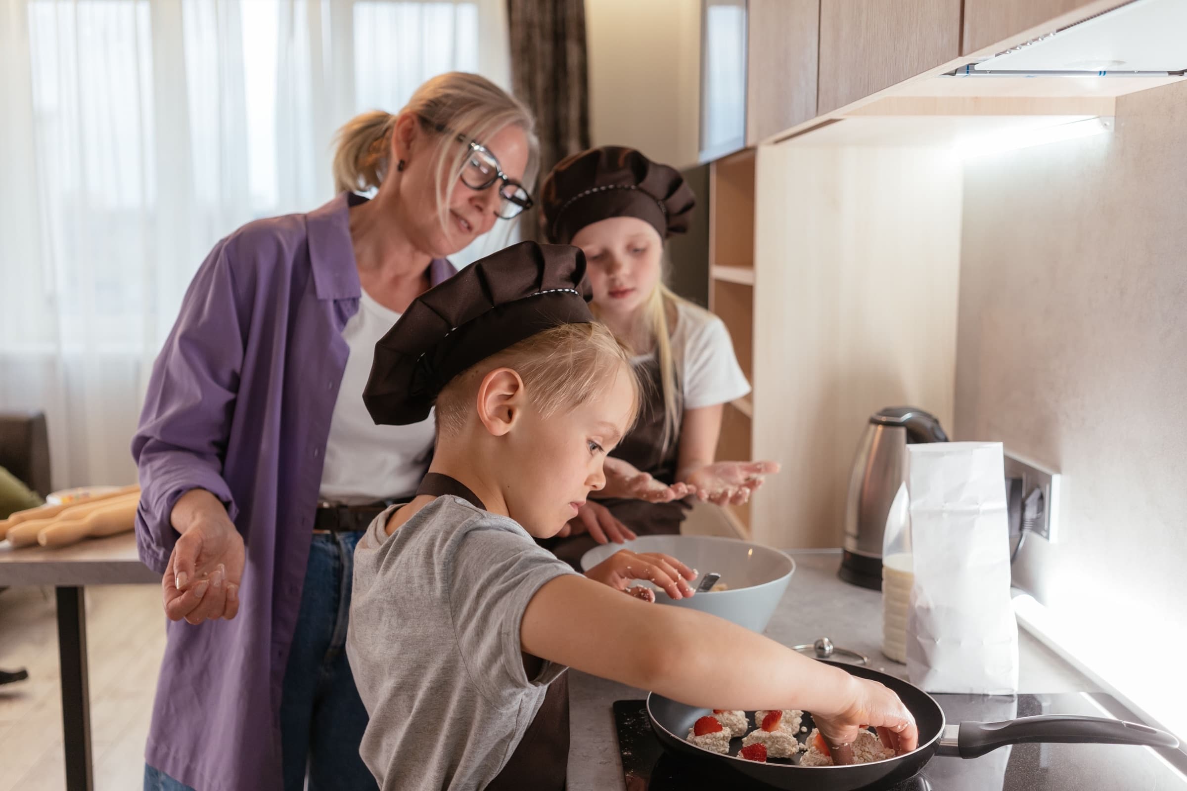 An older woman and two children making something at a kitchen counter
